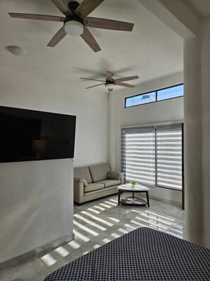Uma sala de estar espaçosa com ventilador de teto, sofá, mesa de centro e janelas amplas com persianas.