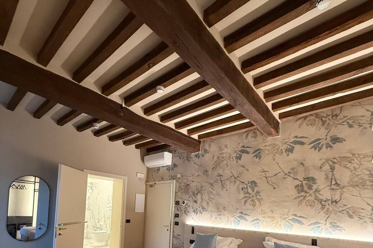 A bedroom with two beds, wooden beams on the ceiling, a floral wallpaper, and a mirror on the wall.