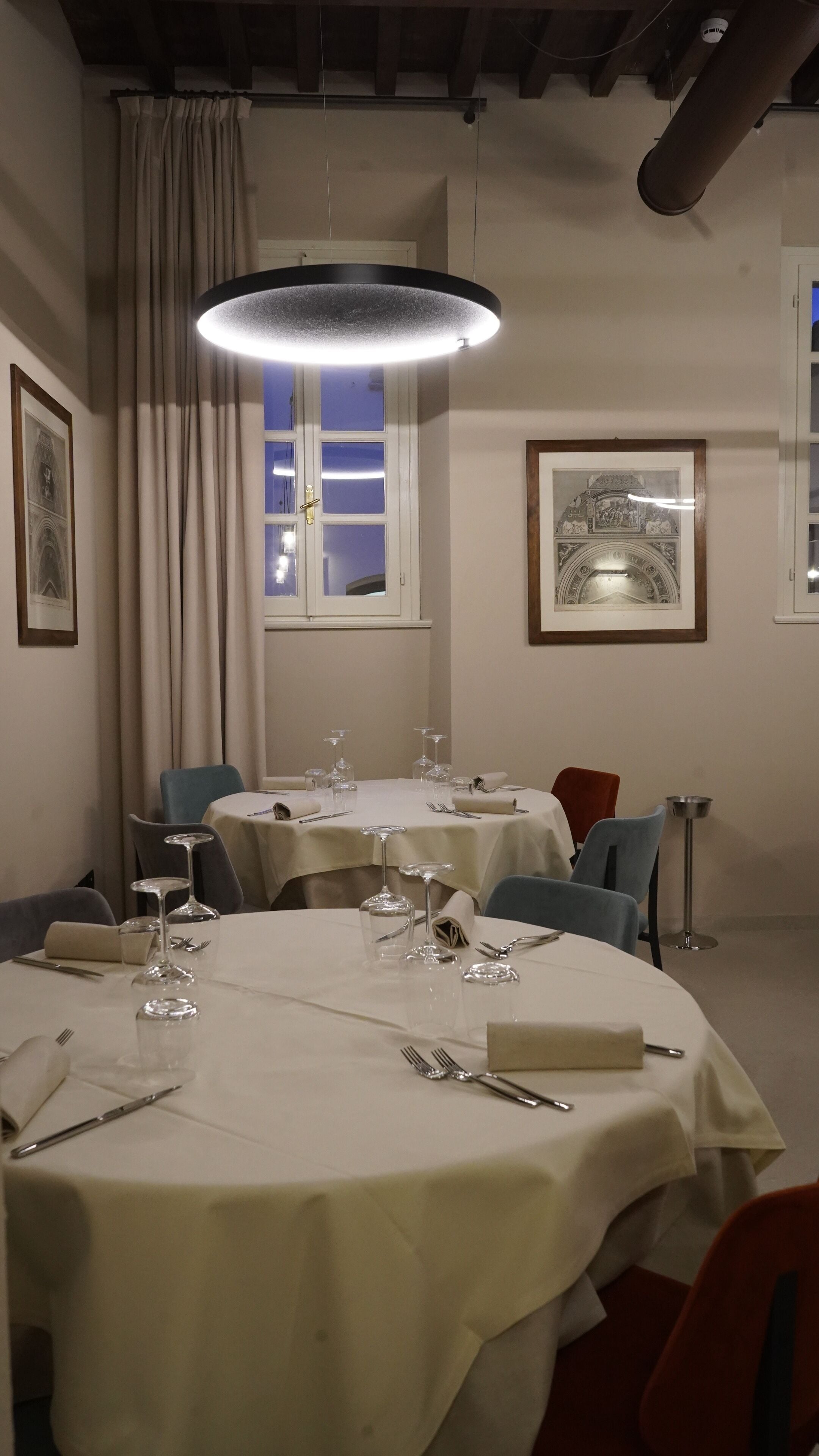 A dining area with round tables set for a meal, featuring white tablecloths, cutlery, and wine glasses.