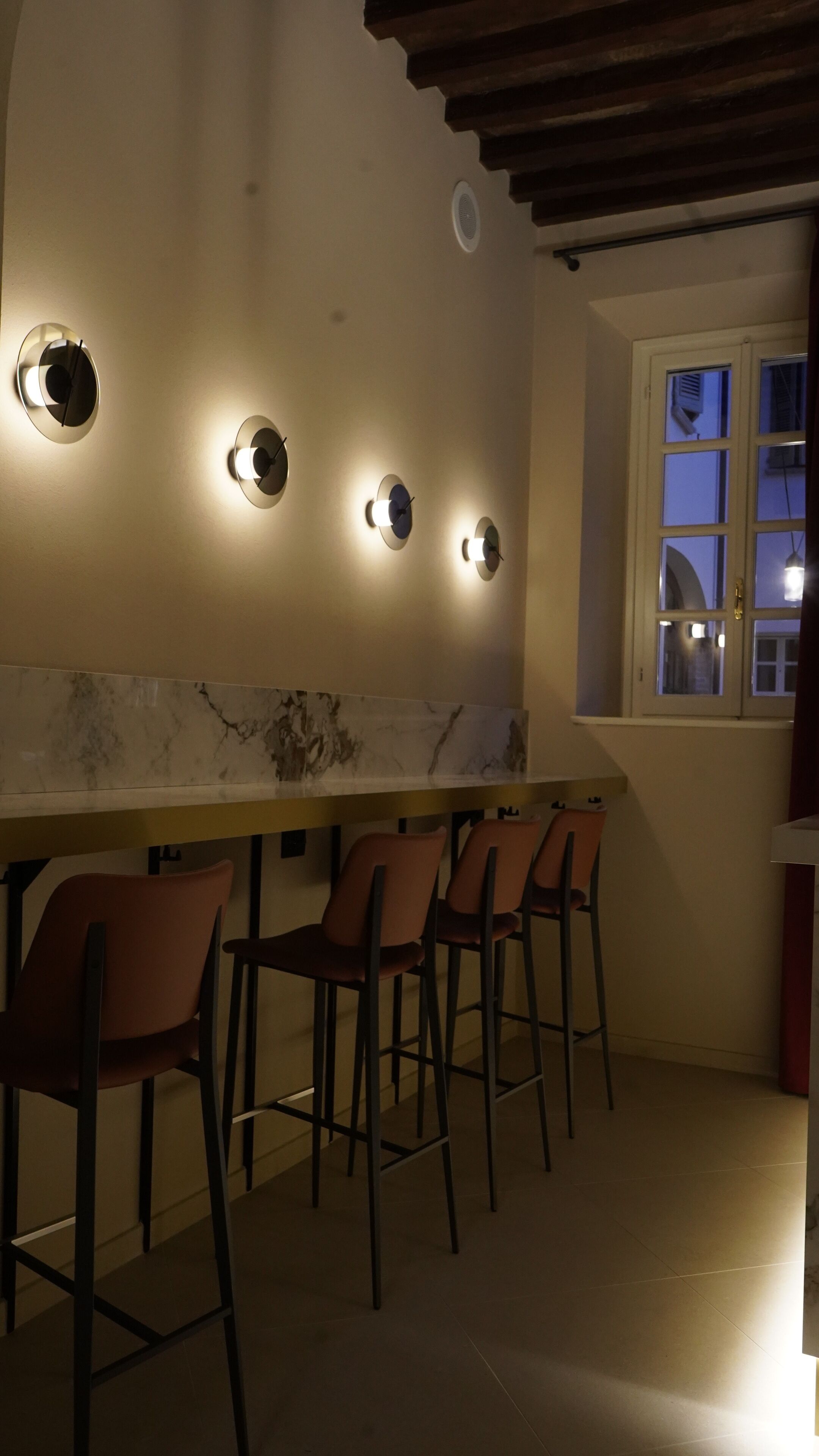 Una cocina con encimera de mármol, cuatro taburetes de bar y lámparas fijadas a la pared.