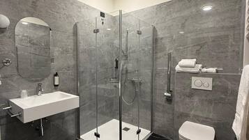 A modern bathroom with a glass-enclosed shower, a white sink, and a toilet.