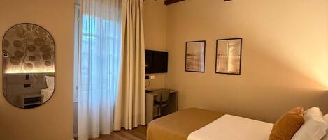 Un dormitorio con techo de madera, cama con ropa de cama blanca y marrón, un escritorio con silla y dos cuadros en la pared.