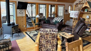 Interior acogedor de una cabaña con chimenea, muebles de madera y ventanas amplias.