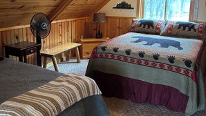 Un dormitorio acogedor en el ático, con techo inclinado, una cama con colcha estampada, un escritorio con silla y un ventilador de pie.