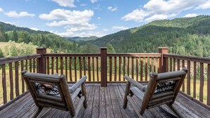 Una terraza de madera con dos sillas frente a una vista panorámica de un valle boscoso bajo un cielo despejado.