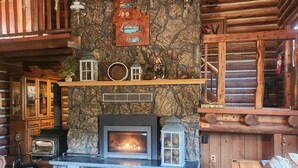 Interior acogedor de una cabaña de troncos con chimenea de piedra, muebles de madera y decoración rústica.