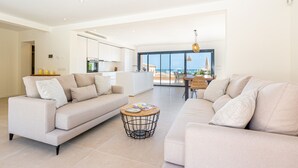 Een moderne woonkamer met twee banken, een salontafel en uitzicht op zee door grote ramen.