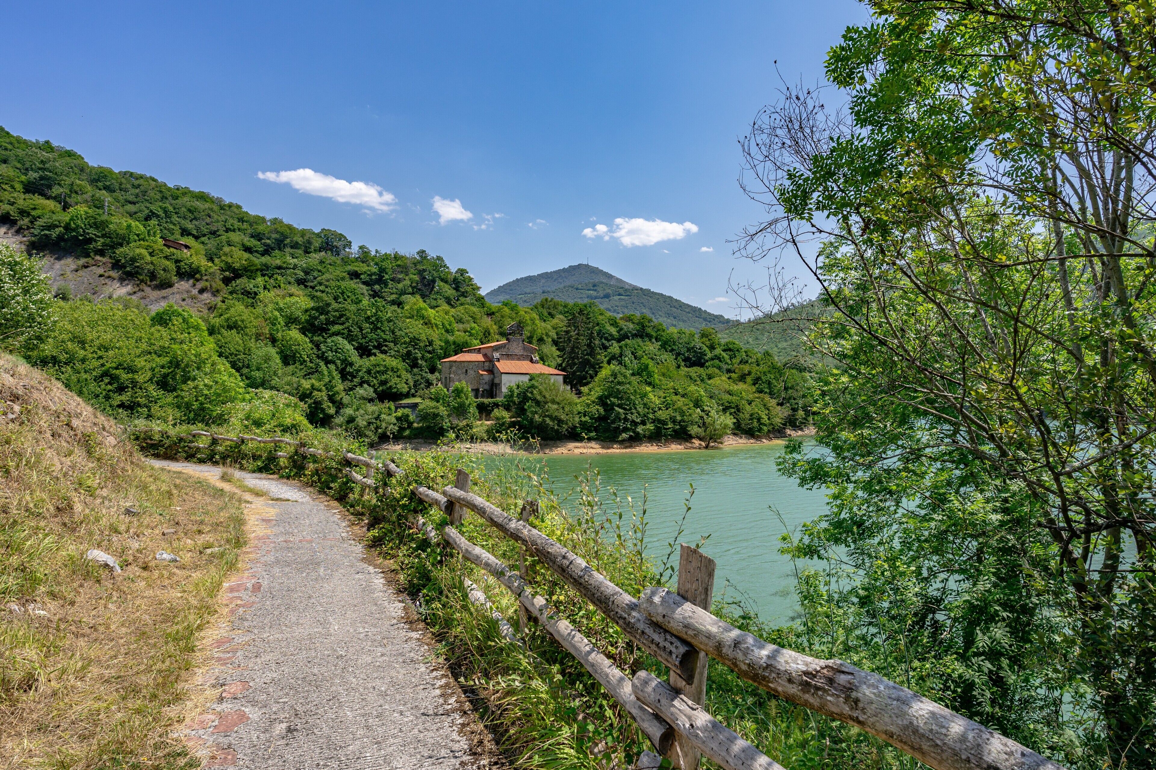 Ein Weg führt zu einem Haus mit rotem Dach, umgeben von üppigem Grün und einem Berg im Hintergrund.