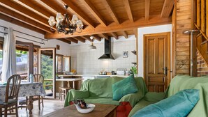 A cozy living area with a wooden ceiling, a green sofa, a wooden coffee table, and a kitchen in the background.