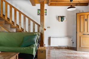 Un escalier en bois mène à un canapé vert, un radiateur et une porte dotée d’une poignée.