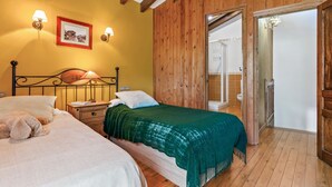 A bedroom with two beds, wooden walls, a wooden ceiling, a picture on the wall, and a bathroom visible through an open door.