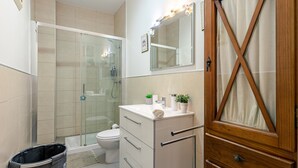 Un bagno con box doccia in vetro, un water, un mobile lavabo con specchio e un armadietto in legno.