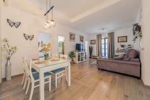 Uma sala de estar ampla com sofá, mesa de jantar, cadeiras e televisão.
