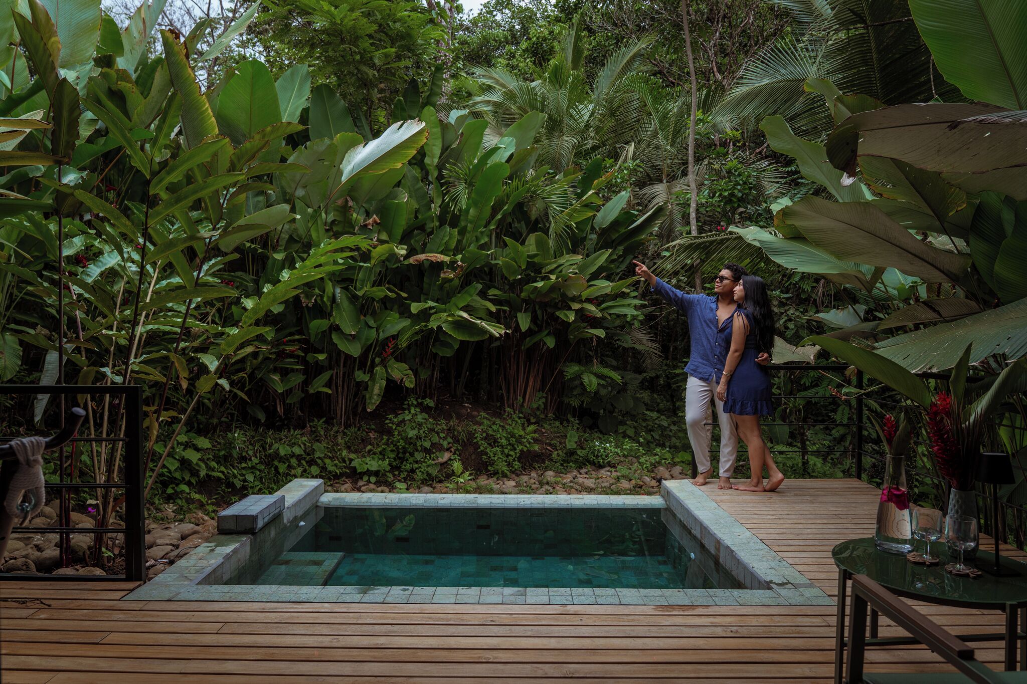 A wooden deck with a pool, surrounded by lush tropical vegetation.