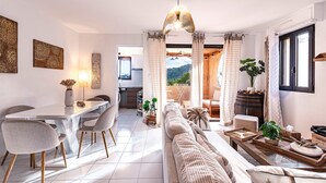 Un salon moderne avec un canapé, une table à manger et des chaises. On aperçoit une cuisine et un balcon agrémenté de plantes.