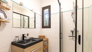 Une salle de bain avec un meuble-lavabo en bois, une cabine de douche en verre et une petite fenêtre.