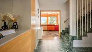 En modern interiör med en receptionsdisk, en trappa med marmorgolv och utsikt över omgivningen genom ett stort fönster.