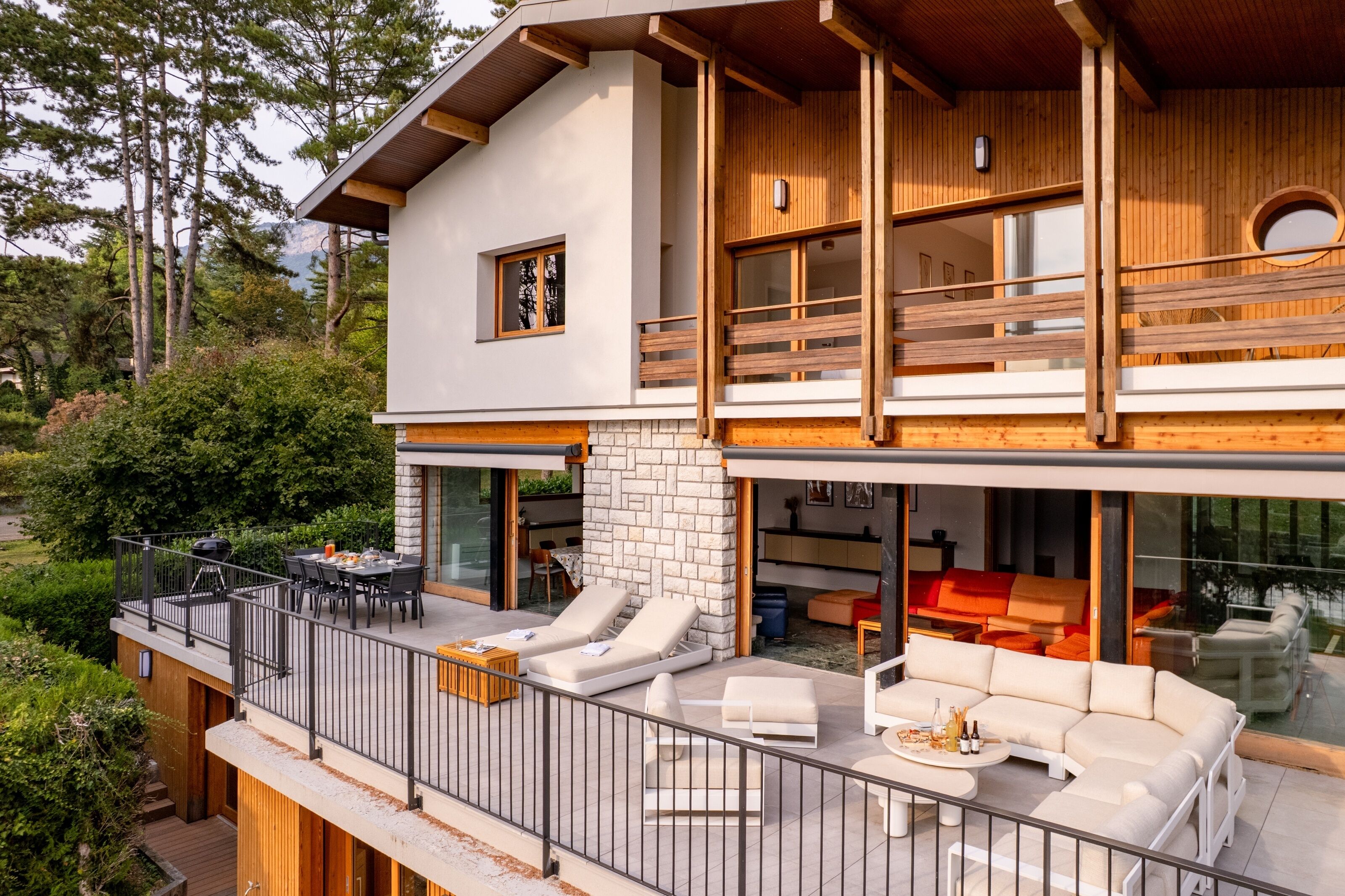 Une maison moderne à deux étages, dotée d’un balcon, d’un espace salon extérieur et d’une cheminée.