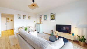 Ein modernes Wohnzimmer mit einer Couch, einem Esstisch, Stühlen, einem Fernseher und Kunstwerken an den Wänden.