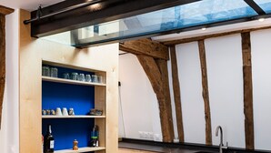 A kitchen with a black marble table, wooden chairs, a blue shelf with kitchen items, and exposed wooden beams. - Le Saint Claude - Studio dans le Marais (Paris)