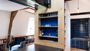 A room with a wooden table, bookshelves, a blue accent wall, and a hanging light fixture. - Le Saint Claude - Studio dans le Marais (Paris)