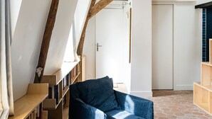 A cozy reading nook with a blue chair, wooden bookshelves, and exposed wooden beams. - Le Saint Claude - Studio dans le Marais (Paris)