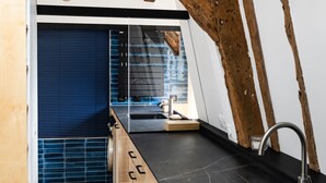 A modern kitchen with exposed wooden beams, a black countertop, and a built-in sink. - Le Saint Claude - Studio dans le Marais (Paris)