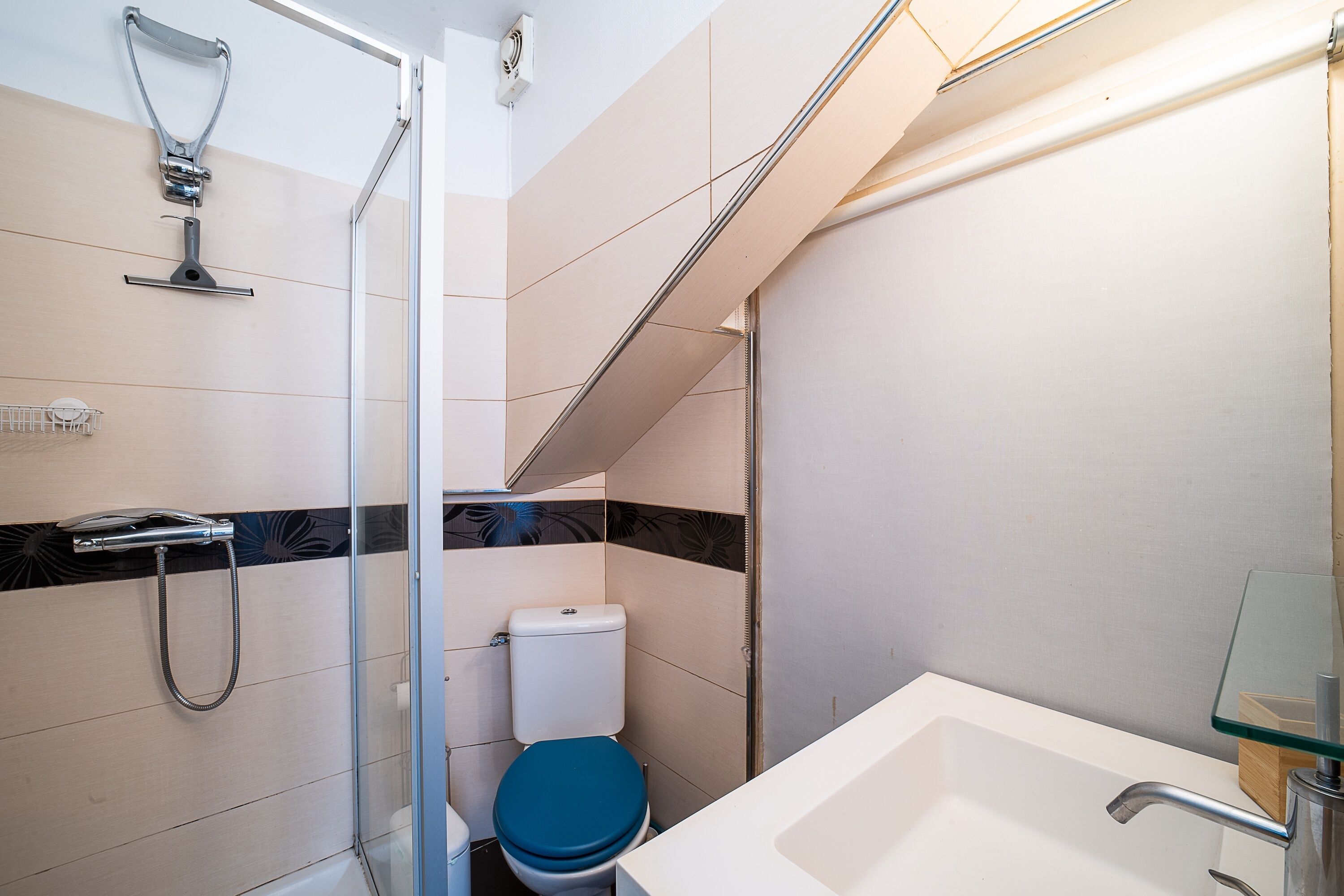 Une salle de bain moderne avec une douche à parois de verre, un lavabo blanc et des toilettes bleues.