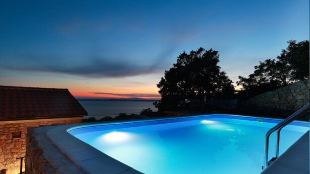 En swimmingpool med en stenmur och utsikt över solnedgången.