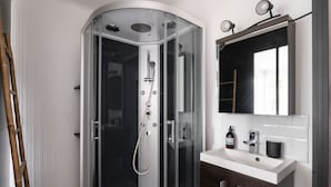 A modern bathroom with a glass-enclosed shower, a white sink with dark wooden cabinets, and a mirror above the sink.