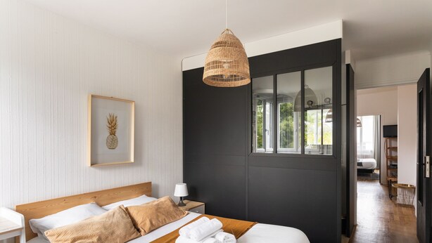 A modern hotel room with a large bed, a bedside table, a lamp, and a framed picture on the wall.