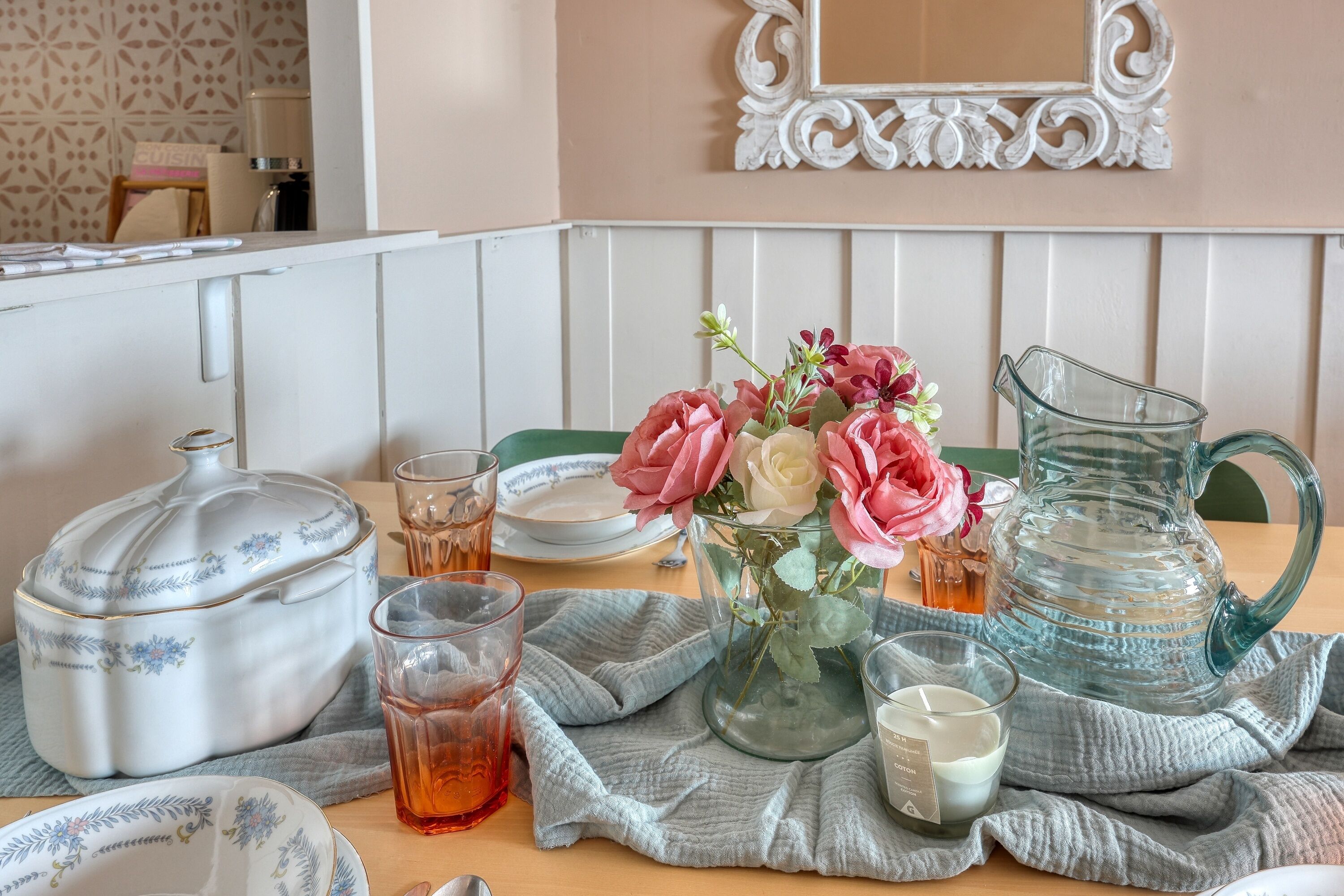 A table set with a teapot, cups, a pitcher, a candle, and a vase with flowers.