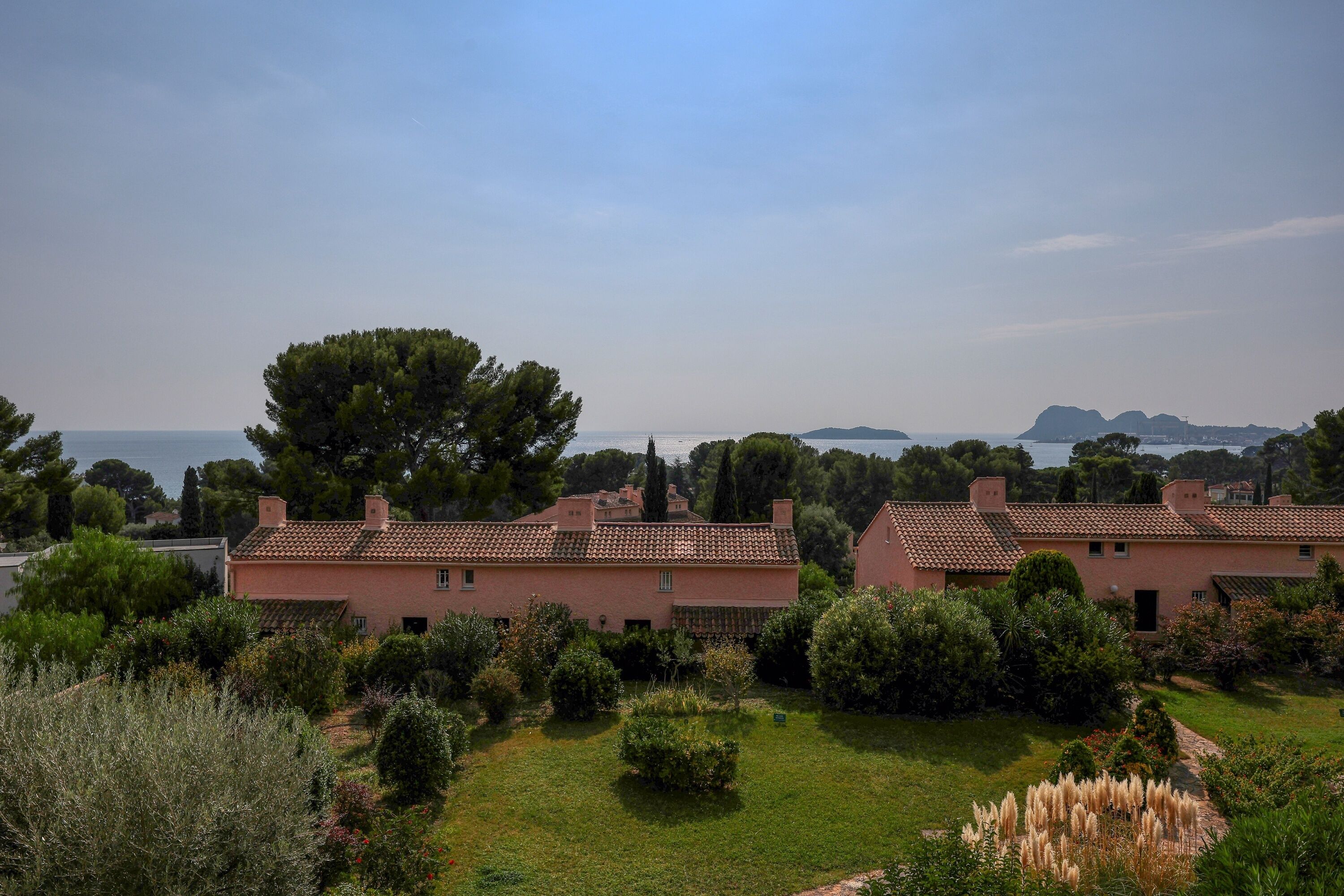 Una villa con jardín, vistas al mar y una cadena montañosa distante.