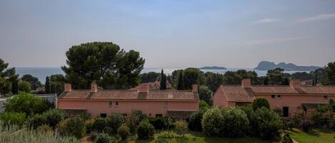 Una villa con jardín, vistas al mar y una cadena montañosa distante.