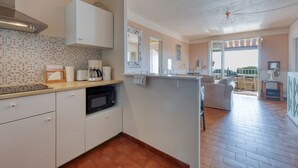 Una cucina moderna con mobili bianchi, un forno a microonde e una macchina da caffè. C'è un'area pranzo con un divano e vista sull'esterno.