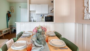 Un'area pranzo con tavolo apparecchiato per quattro persone, un vaso con fiori e una cucina sullo sfondo.