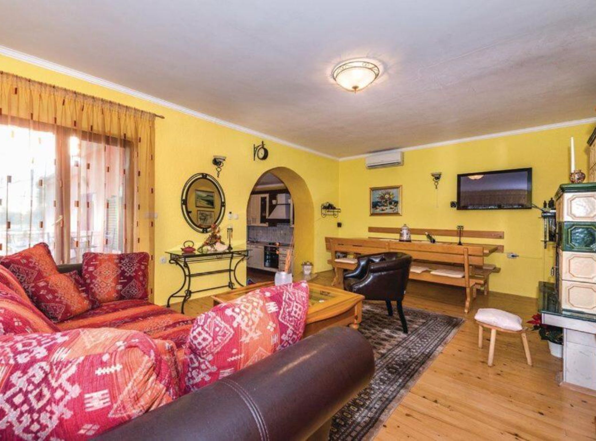 A living room with a sofa, a coffee table, and a TV. There is a kitchen visible through an archway.