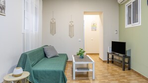 A living room with a green sofa, a small white table with a plant, a TV on a stand, and a wall-mounted air conditioner. - Apartment 'La Bella Escondida' with Wi-Fi and Air Conditioning (Cadiz)