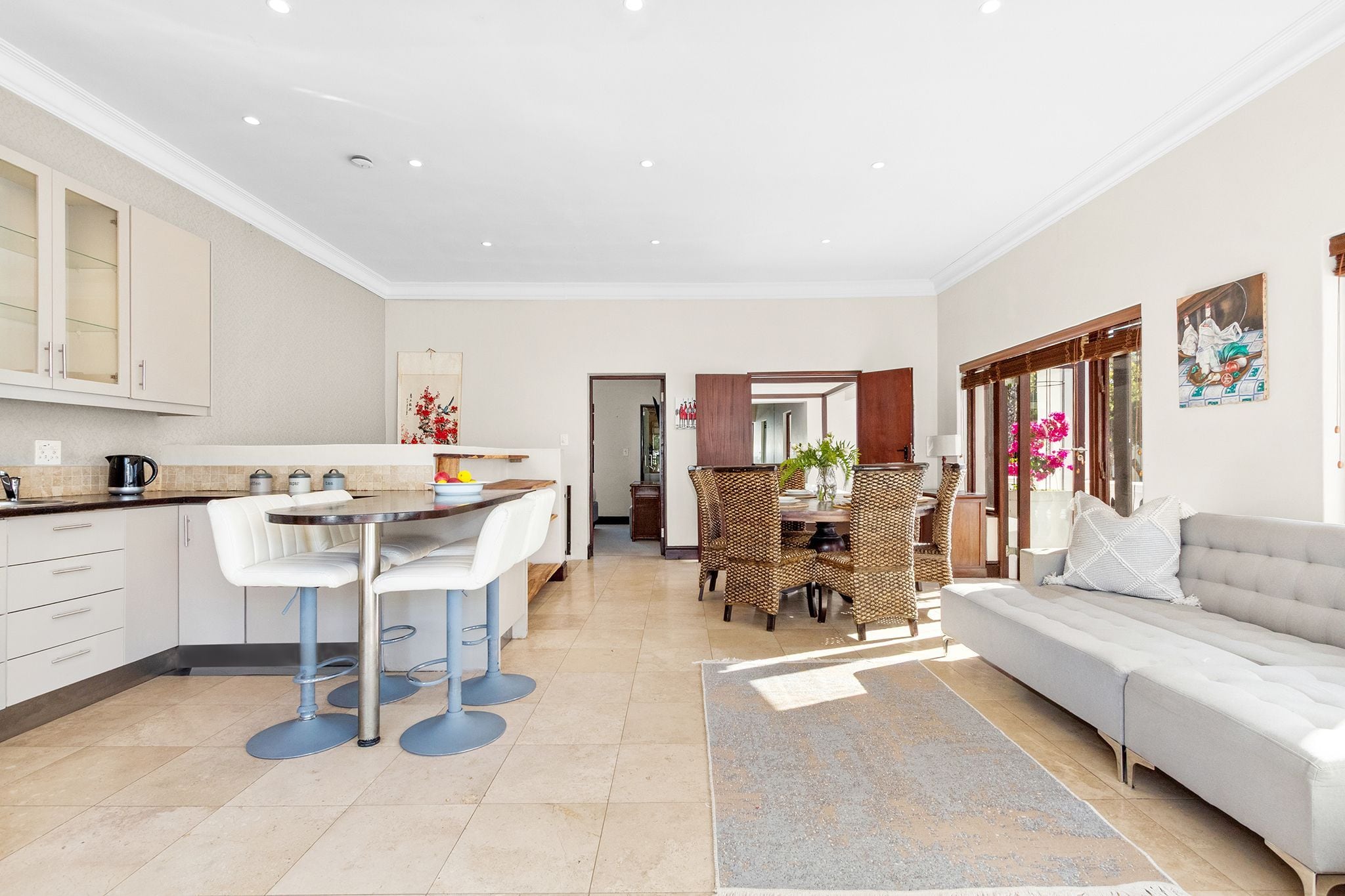 A modern kitchen with white cabinets, a dining area with a round table and chairs, and a living area with a sofa and a rug.