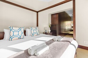 Moderni hotellihuone, jossa on suuri sänky, kaksi koristeellista tyynyä, yöpöytä lampun kanssa ja näkymä hissiin.