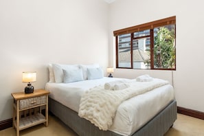 A bedroom with a bed, two nightstands, a window, and a view of buildings and trees outside. - Villa 17 on Graham (Cape Town)
