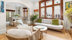 A spacious living area with wicker furniture, a white sofa, and a large window with wooden frames. - Villa 17 on Graham (Cape Town)