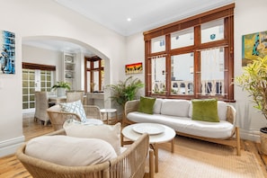 A spacious living area with wicker furniture, a white sofa, and a large window with wooden frames. - Villa 17 on Graham (Cape Town)