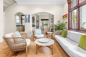 A spacious living area with a white sofa, wicker chairs, a round coffee table, and a view of the kitchen through an archway. - Villa 17 on Graham (Cape Town)
