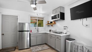 Une cuisine moderne avec des meubles gris, un réfrigérateur en acier inoxydable, un four à micro-ondes et un téléviseur fixé au mur.