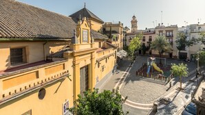 Un bâtiment historique doté d’un toit en tuiles, d’une cour intérieure avec un espace de jeux et, en arrière-plan, d’un clocher.