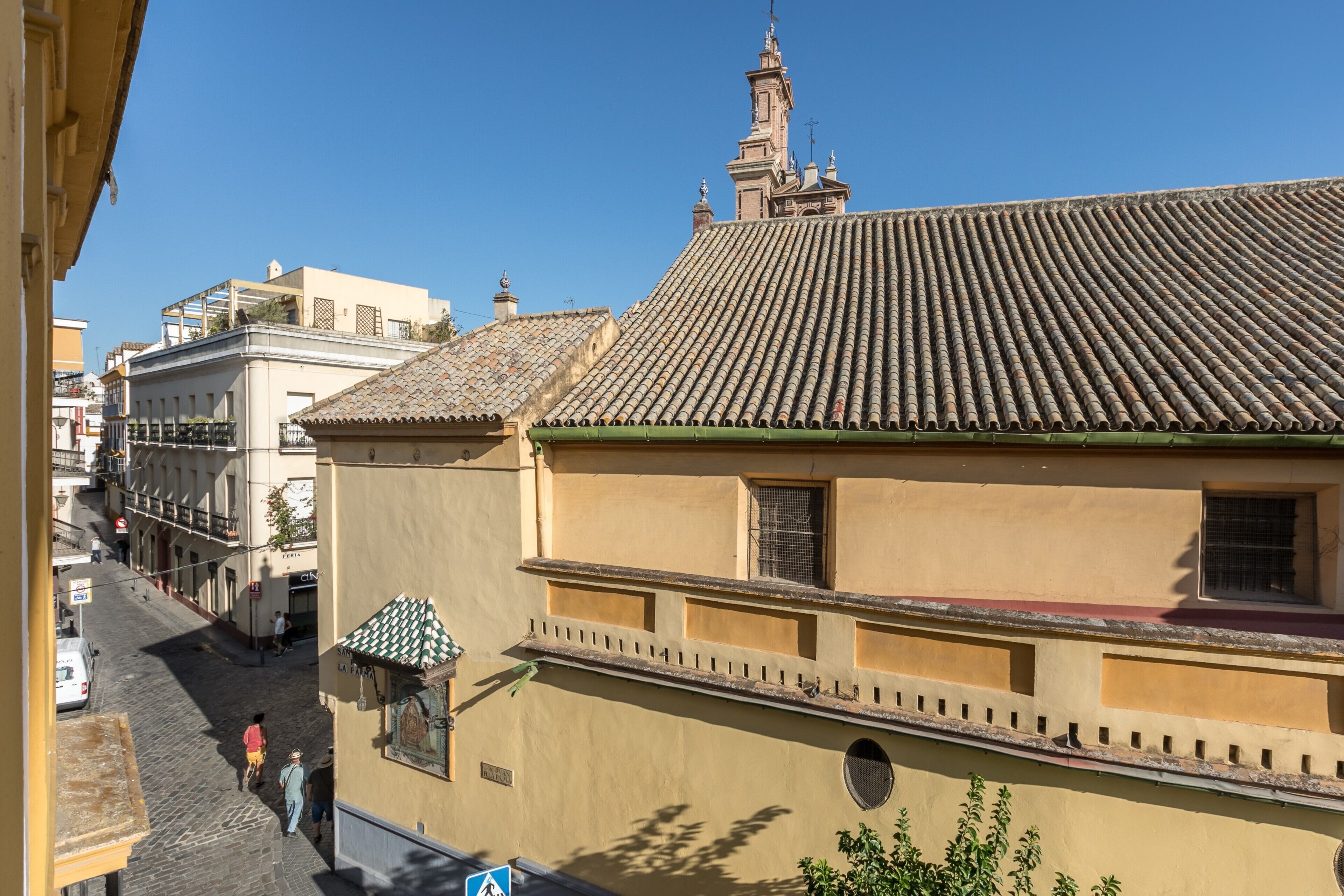 Une vue de rue avec des bâtiments, un ciel dégagé et quelques piétons.