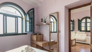 Une chambre à coucher avec un lit, un bureau en bois, un miroir et une vue sur un balcon équipé d’un canapé.