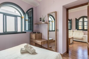 Et soveværelse med seng, et træskrivebord, et spejl og udsigt til en balkon med sofa.