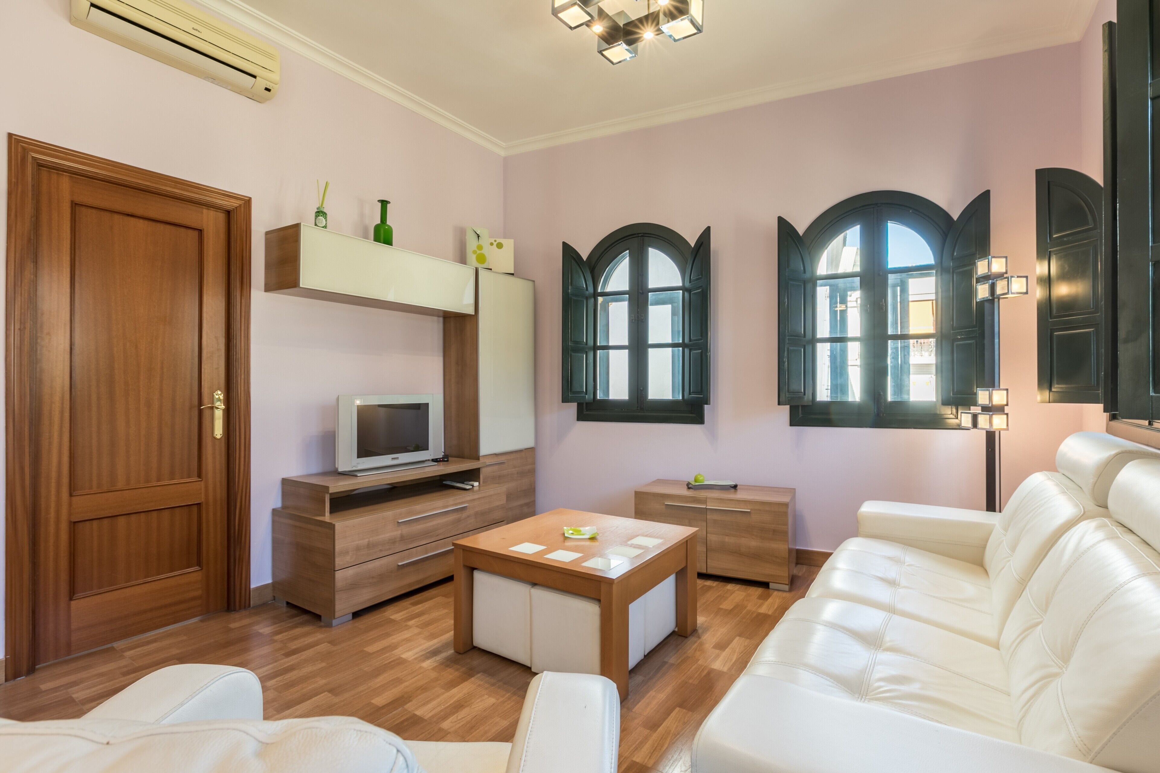 Un salon moderne avec une porte en bois, un téléviseur, un canapé blanc, une table basse en bois et une fenêtre à sommet en arc de cercle.